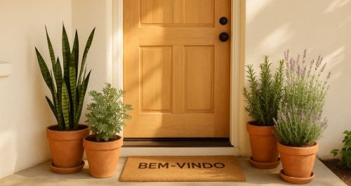 Vasos com espada-de-são-jorge, arruda, alecrim e lavanda ao lado de uma porta clara com tapete “BEM-VINDO”, simbolizando proteção e boas-vindas na entrada da casa.